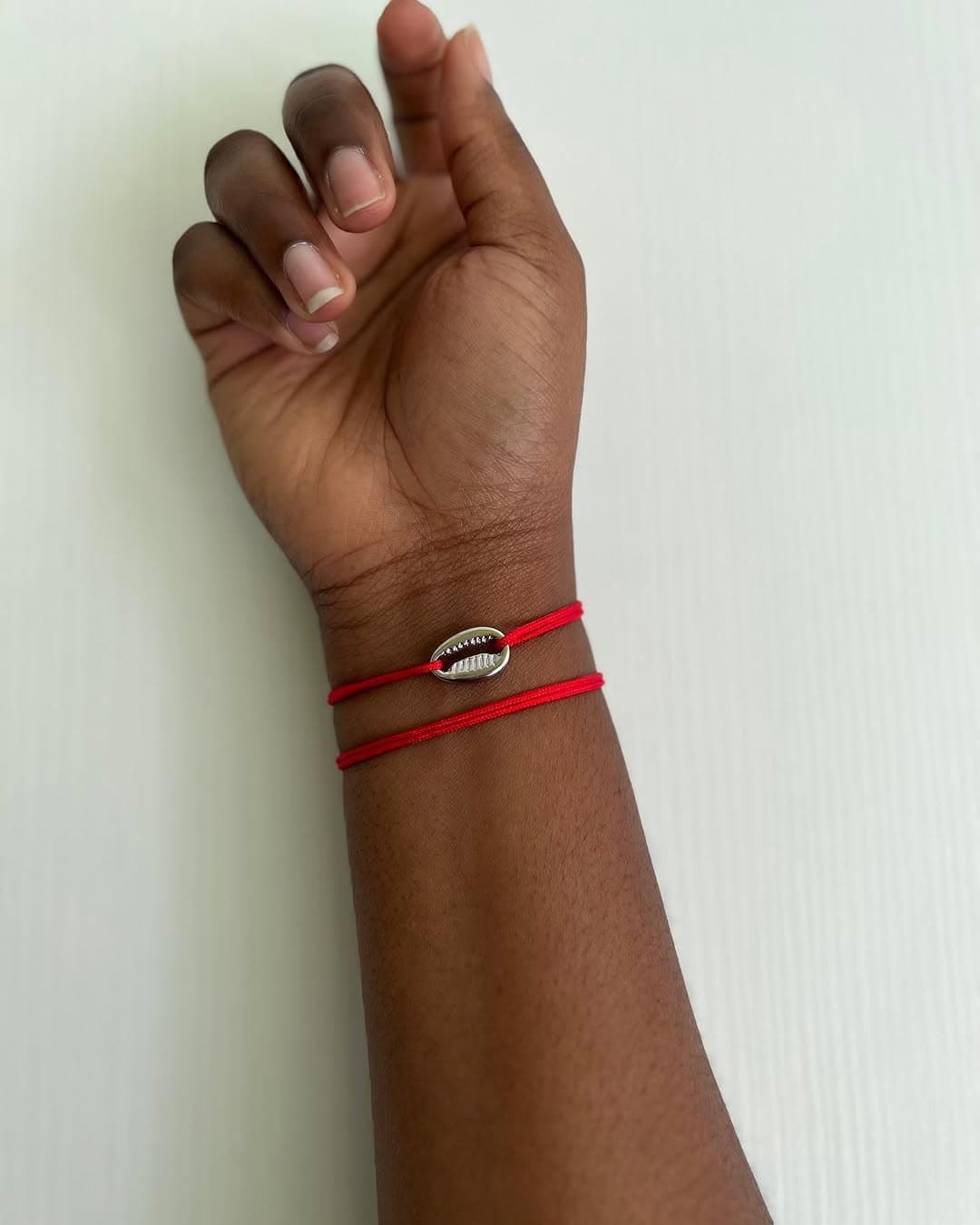 Bracelet cauris sur cordon rouge porté au poignet